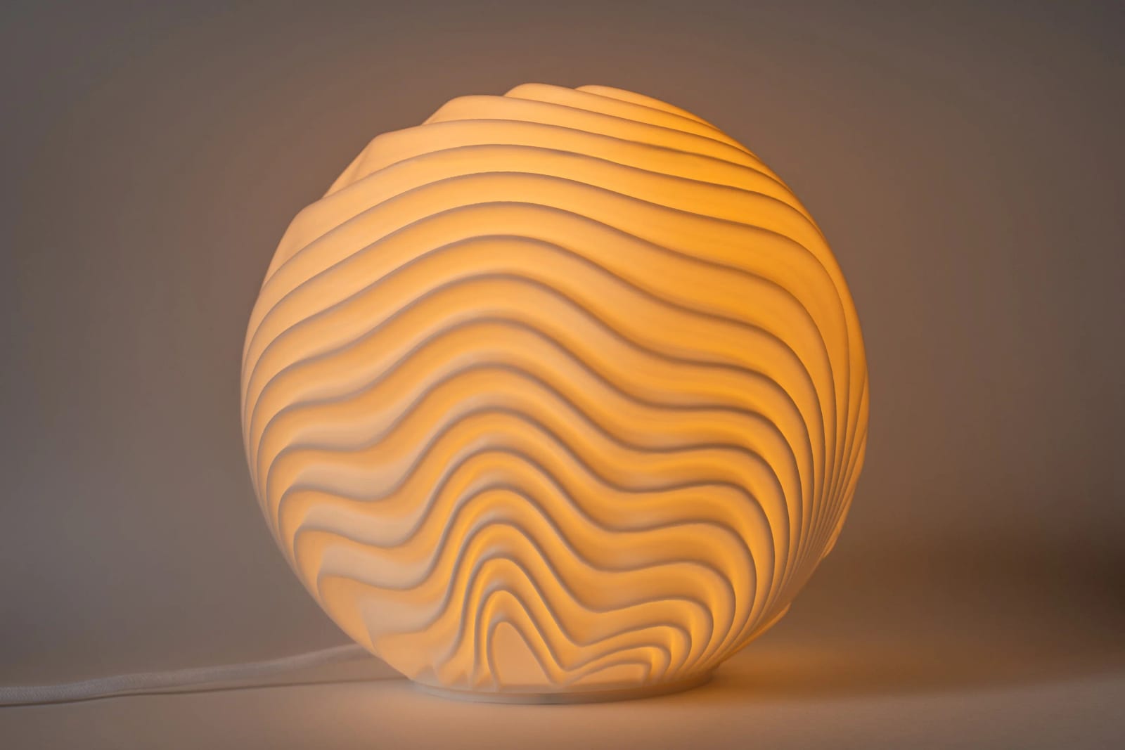 Den 3D-printade lampan Dyn med ljuset tänt: den krusade ytan lyser varmt mot en grå bakgrund