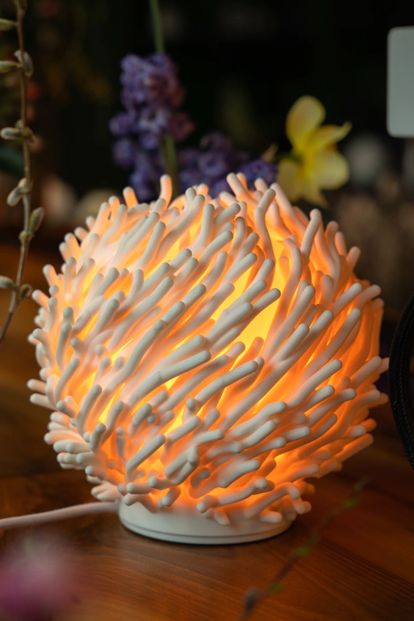 A Leora lamp, lit, on a wooden table among spring flowers